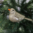 A glittery gold bird ornament with an orange beak sits on lush green pine branches, creating a festive and joyful holiday atmosphere.
