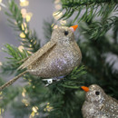 Glittery gold bird ornaments with orange beaks perch on a Christmas tree branch, surrounded by warm, soft fairy lights, creating a festive ambiance.