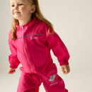A young child with long hair smiles while wearing a bright pink rain suit with hood. The suit has playful cloud graphics, conveying joy and outdoor readiness.
