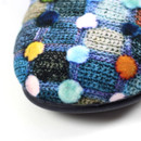 Close-up of the toe area of a Lunar mule slipper, showcasing a soft fabric upper with a multicoloured spot pattern on a knitted-look background. The sole is black and slightly raised, with visible stitching along the edge.