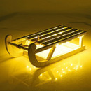 A wooden sled adorned with warm LED lights, casting a soft glow on a reflective surface, set against a yellow background.
