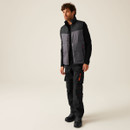 Full-body view of male model in workwear outfit with insulated vest, black long sleeve shirt, cargo trousers, and safety boots, showcasing functional industrial apparel