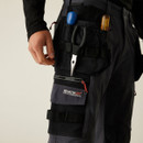 Side detail of utility work trousers with attached tool pouch, pliers holder, zip cargo pocket, and “Regatta Professional” branding, designed for tradesmen and construction work.
