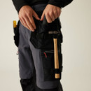 Detail of multi-pocket tool holster on work trousers holding hammer and screwdriver, with secure straps, zip pocket, and ergonomic storage design for professional tradesmen.