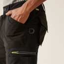 Side detail of black cargo work trousers with D-ring attachment, deep utility pocket, zip thigh pocket with neon green accent, and rugged construction for jobsite performance.