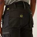 Rear close-up of black technical work pants showing elastic waistband, back pocket with flap, neon green logo detail, and reinforced stitching for durability and flexibility.