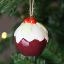 A close up view of a ceramic Christmas pudding with holly and berries on top, hanging from a Christmas tree.