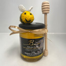 A jar of Welsh honey with a cute knitted bee and a honey dipper tied with a gold ribbon. The scene feels charming and artisanal.