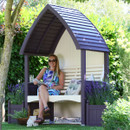 Lavender and cream painted garden arbour under trees, with a woman seated on the bench and matching side planters filled with lavender.