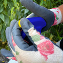 Hands in floral-patterned gardening gloves hold a blue and yellow spray bottle, with green foliage in the background, conveying a gardening theme.