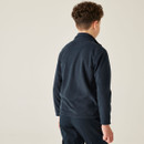 A child with curly hair, seen from behind, wearing a navy fleece jacket and matching pants, stands against a plain beige background.