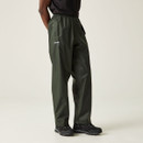 A person in a black shirt and dark green, loose-fitting trousers stands with hands in pockets. They wear black shoes on a plain, light background. A person in a black shirt and dark green, loose-fitting trousers stands with hands in pockets. They wear black shoes on a plain, light background.