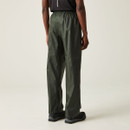 Person wearing green rain trousers and a black shirt, standing with back facing the camera against a neutral background. The mood is casual and minimalistic. Person wearing green rain trousers and a black shirt, standing with back facing the camera against a neutral background. The mood is casual and minimalistic.