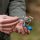 A person holds a compact camping stove, adjusting its removable burner assembly in an outdoor setting.