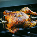 Close-up of a browned roast chicken cooking on a rotisserie spit.