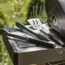 Barbecue tools laid on a side shelf, including tongs and a spatula, beside an open grill.