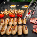Close-up of tongs turning sausages on a hot grill with tomatoes, mushrooms, bacon and fried eggs.