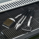 Barbecue tongs, spatula and brass-bristled grill brush laid on grill grates.