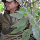 Person in camouflage clothing partially obscured by foliage.