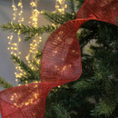 Festive Christmas tree branches wrapped in a glittery red ribbon with warm white fairy lights in the background, creating a cosy holiday atmosphere.