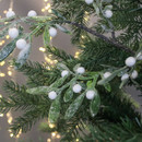 Close-up of frosted mistletoe and pine branches with white berries, surrounded by warm, blurred fairy lights, creating a festive, wintry atmosphere.