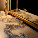 Delicate  leaf wreaths lie on a reflective surface, doubled by a mirror with an ornate golden frame, creating an elegant and serene atmosphere.
