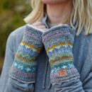 Woman in cosy outdoor setting wears colourful, patterned fingerless gloves. She holds them to her face, conveying warmth and comfort.