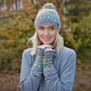 Woman in a colourful knit hat and mittens, wearing a grey jumper. She smiles, standing outdoors with a blurred, autumnal background.