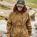 Person in a brown jacket and green cap standing outdoors with rocky terrain in the background.