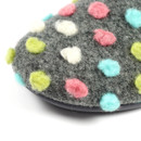 Close-up of a grey woollen slipper showing a soft felt texture with colourful raised polka dots in pastel green, pink, white, and blue. The fabric appears fuzzy and cosy, with the edge of the black sole slightly visible at the bottom.