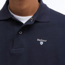 Close-up of a navy blue polo shirt with a collar, featuring the Barbour logo and a small shield emblem on the left chest, worn over a white T-shirt.