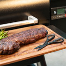 A perfectly cooked, sliced roast rests on a wooden cutting board beside a pair of black kitchen scissors.