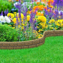 A vibrant flower garden with colourful blooms, including purple, yellow, and orange flowers, is bordered by a low brick wall, surrounded by lush green grass.