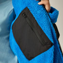 Close-up of a hand holding a vibrant blue fleece jacket, showing a black zippered pocket. The texture appears fluffy and soft.