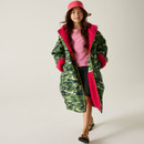 A young girl wearing a green camo coat with pink lining, pink hat, and pink shirt, walks confidently. Her expression is cheerful and relaxed.