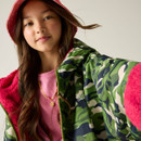 Young girl in a red hat, pink jumper, and green camo jacket takes a selfie. Her expression is calm and relaxed, conveying a casual mood.