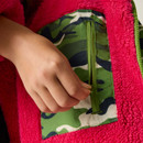 A person zips a green camouflage pocket on a vibrant pink fleece jacket. The close-up highlights textures and contrasts of colours, conveying a playful mood.