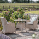 Outdoor wicker garden furniture set with two chairs and a table surrounded by flowering plants.