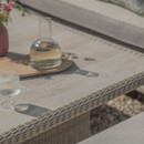 A carafe and glass of white wine on an outdoor table with a wicker edge.