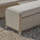 Close-up of a beige wicker garden sofa bench with a cushion on a gravel surface.