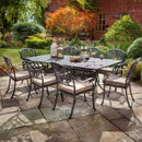 Patio dining set with six chairs in a garden with a brick house and plants in the background.