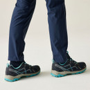Side view of navy and turquoise walking shoes with supportive hiking soles, worn with navy outdoor trousers.