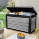 Grey wood-effect garden storage box with black lid, shown open on a patio and filled with outdoor cushions and blankets.