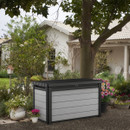 Grey wood-effect garden storage box with black lid placed in a garden beside plants and flowers.