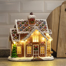 Illuminated gingerbread house Christmas decoration with snow-covered roof, festive icing details, wreaths, candy cane accents, and warm glowing windows displayed on a kitchen worktop.