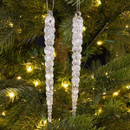 Two elegant acrylic icicle ornaments hanging on a Christmas tree, surrounded by twinkling lights and green branches.