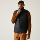 Man wearing a black puffer vest and brown long-sleeve shirt with tan cargo pants and a black cap. He stands against a neutral background. Casual and confident.