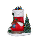 Front  view of a festive elf cottage designed as a red Christmas stocking, featuring a decorated tree, glowing windows and snow-dusted landscaping.