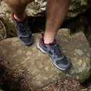 Man standing on a rock wearing grey and black waterproof walking trainers with red accents and rugged soles.