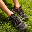 Close-up of grey waterproof hiking shoes with red detailing and secure lace fastening on green grass.